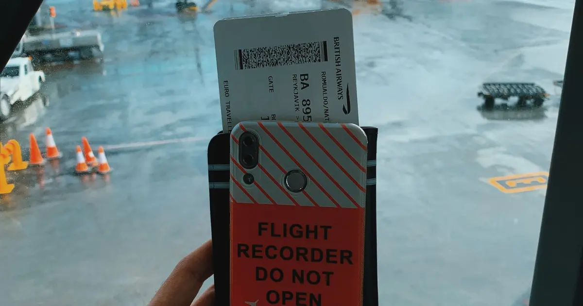 Traveler holding a smartphone and boarding pass at an airport window